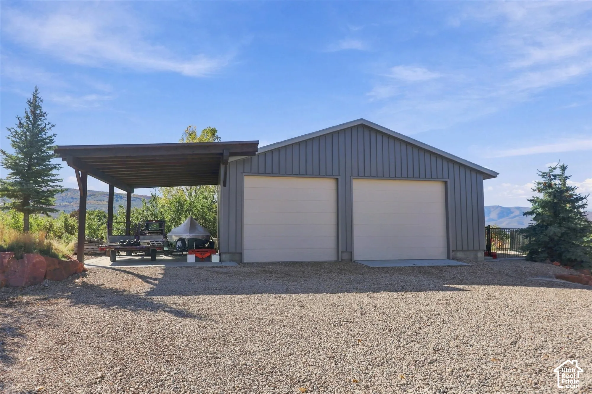 Detached metal-sided garage featuring two garage bays, a covered side carport, and a gravel driveway