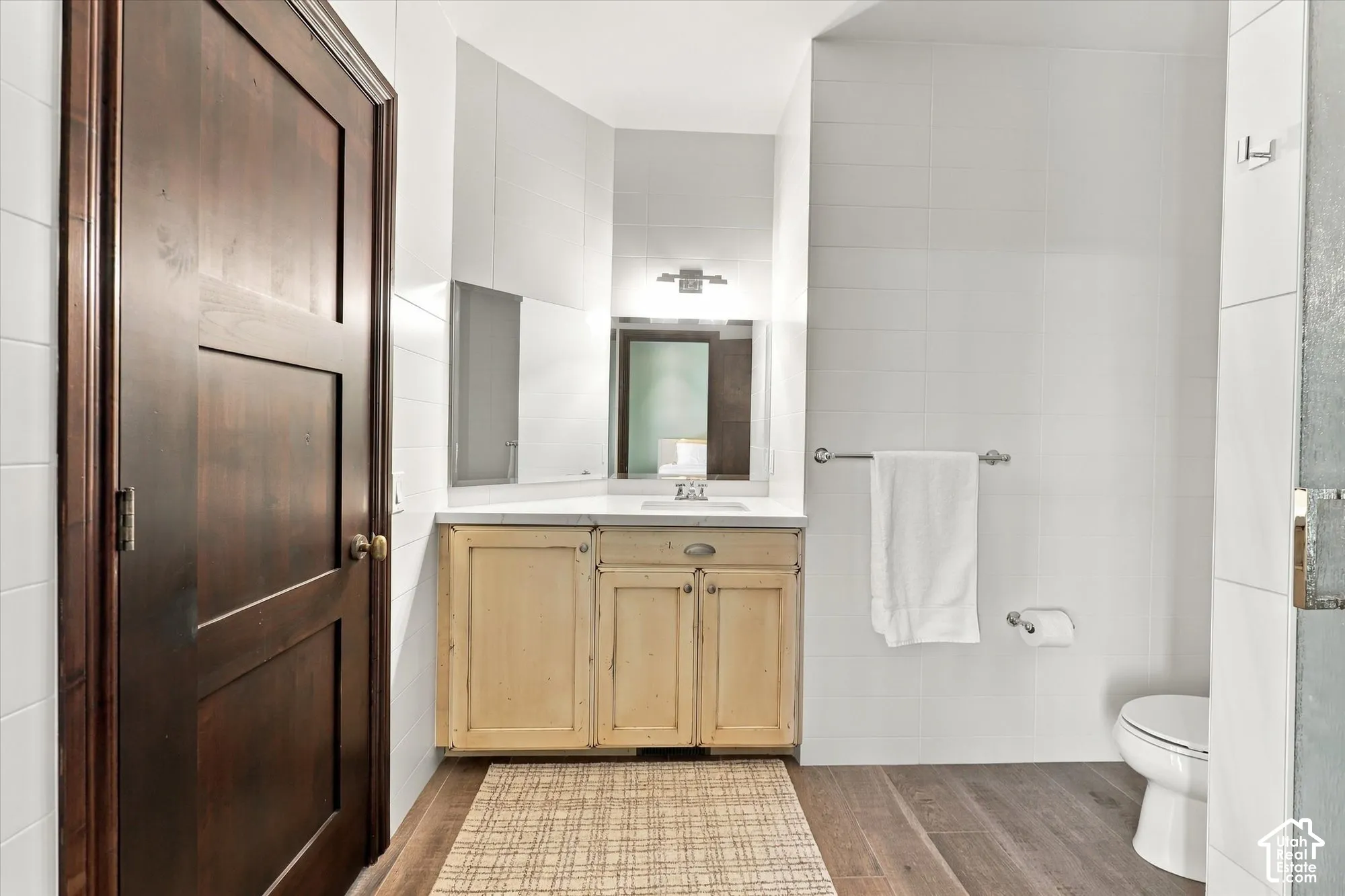 Bathroom featuring a vanity with light wood-tone cabinetry, solid surface countertop, rectangular under-mount sink, wood-finish flooring, and white tiled walls