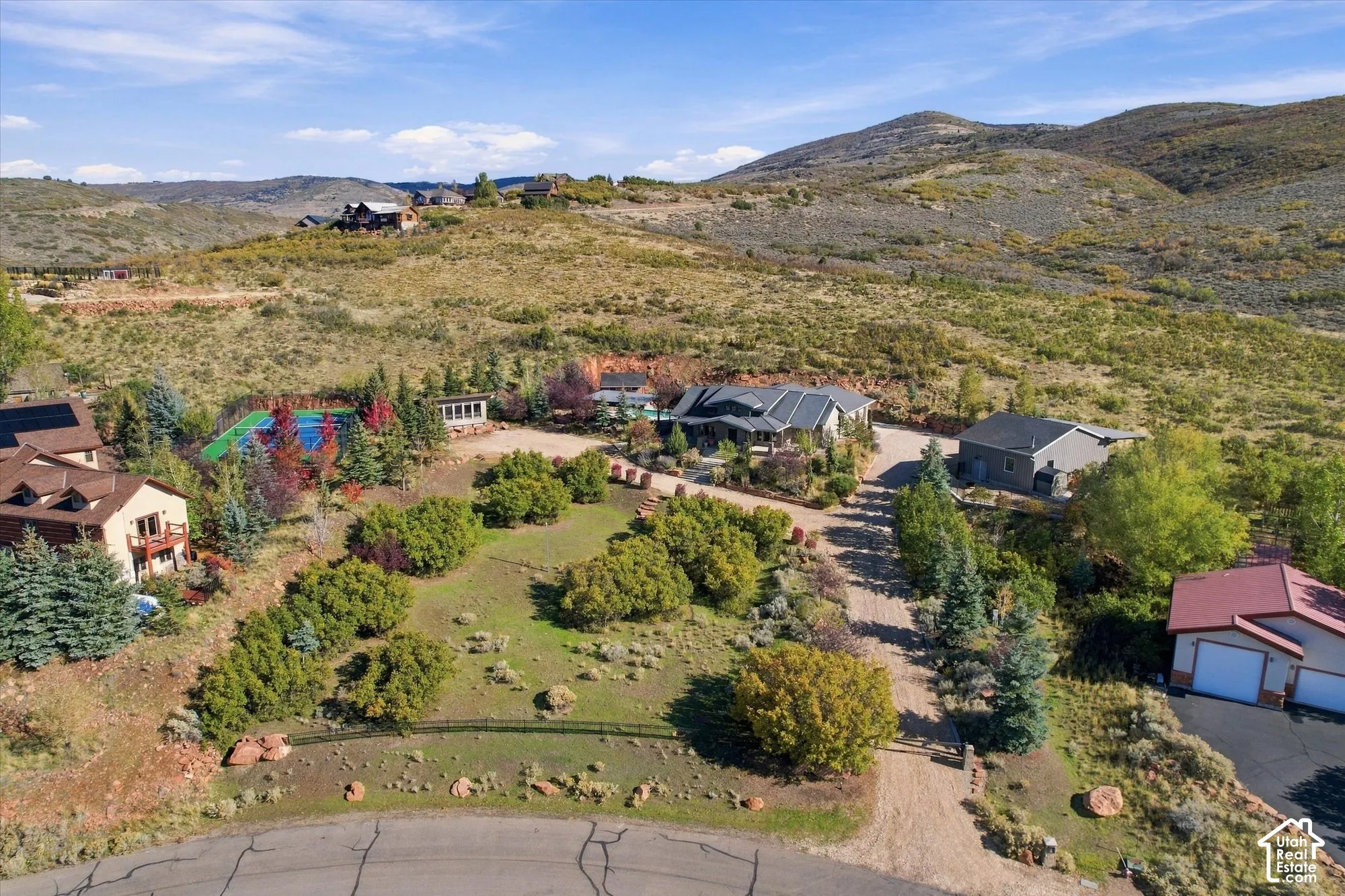 Extensive multi-structure property featuring a tennis court, swimming pool, detached garage, and mountain backdrop