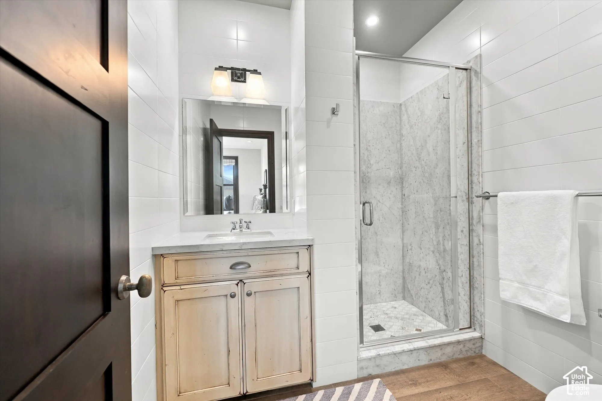 Bathroom featuring white subway tile walls, a wood-finish vanity with a stone countertop, a glass-enclosed shower with stone-surround, and recessed lighting