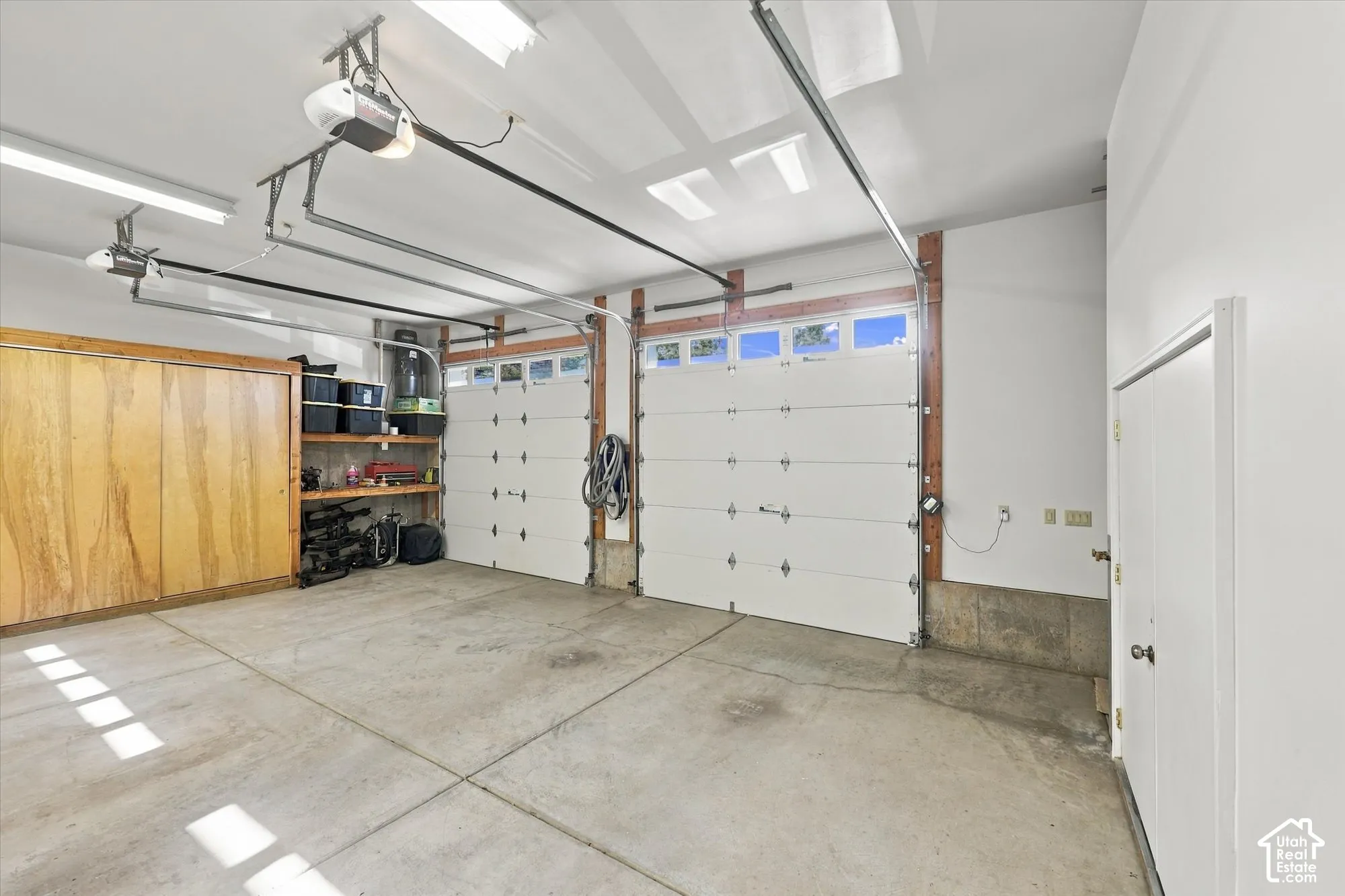 Three-car garage featuring segmented overhead doors with windows, built-in wooden cabinetry, integrated shelving, and ceiling-mounted lighting