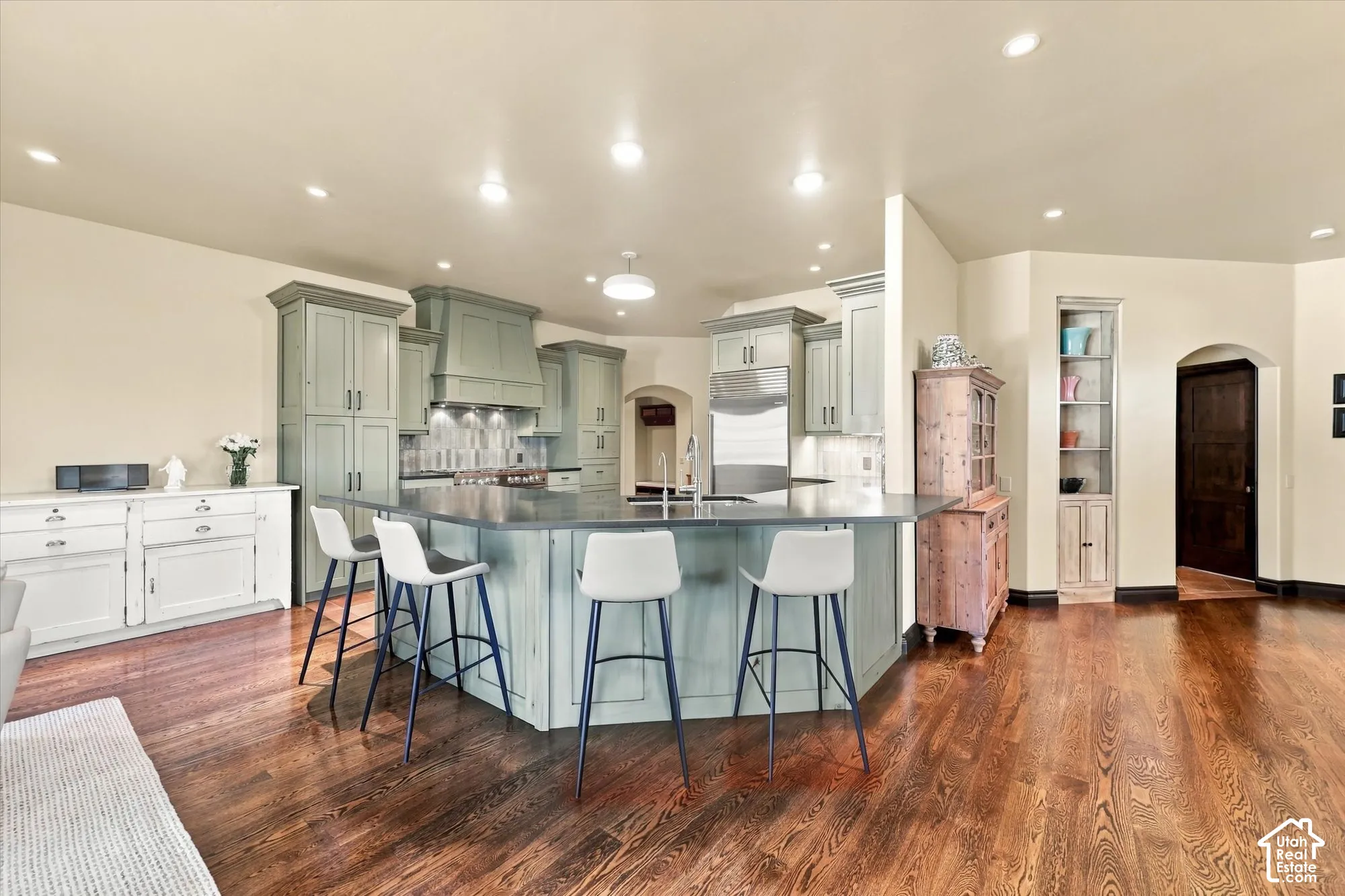 Kitchen featuring sage green cabinetry, a large central island with a dark countertop, recessed ceiling lighting, wood-finish flooring, and built-in shelving