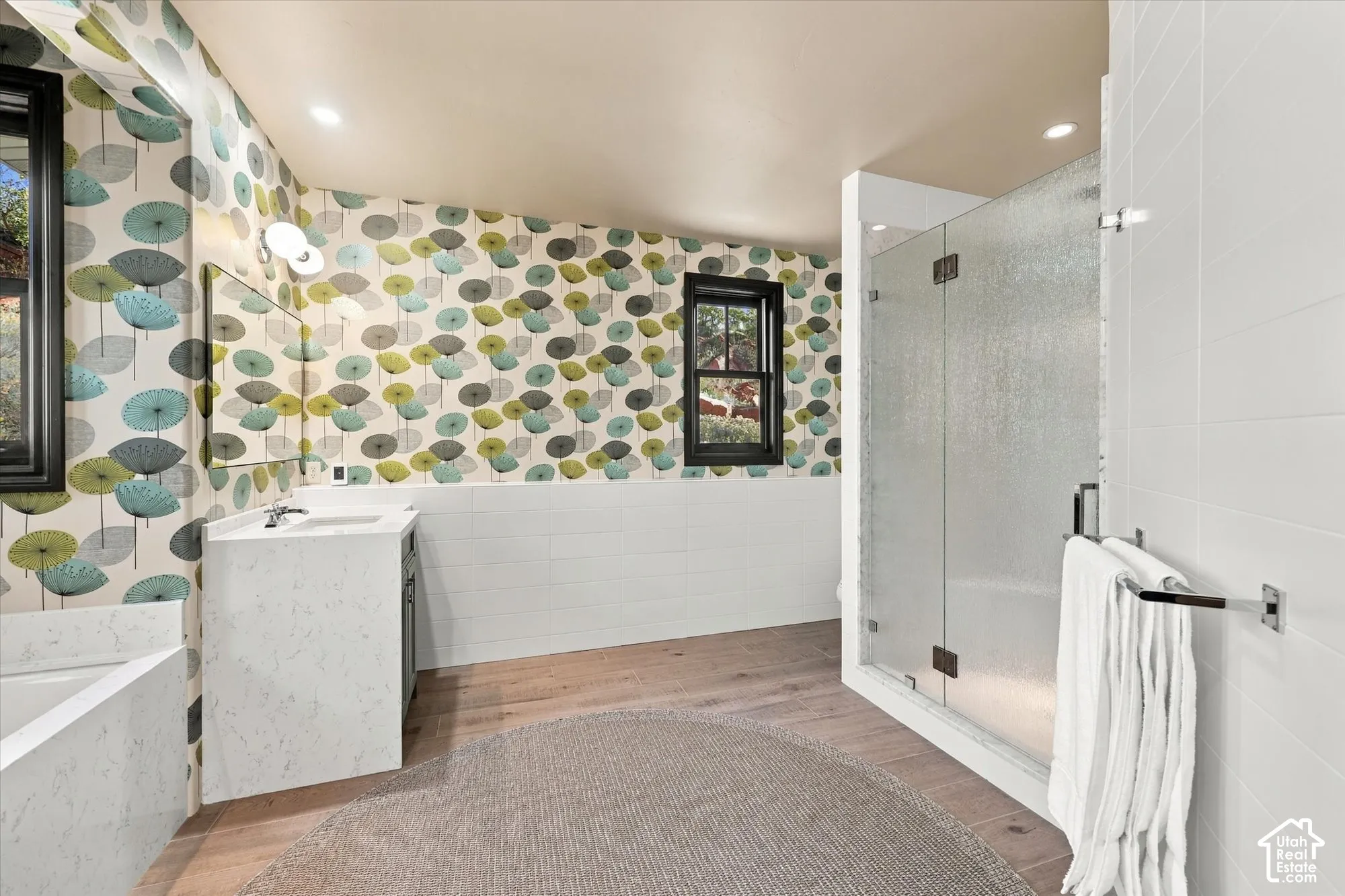Bathroom featuring a quartz-topped vanity, walk-in shower with a glass enclosure, wood-finish flooring, and white subway tile wainscoting