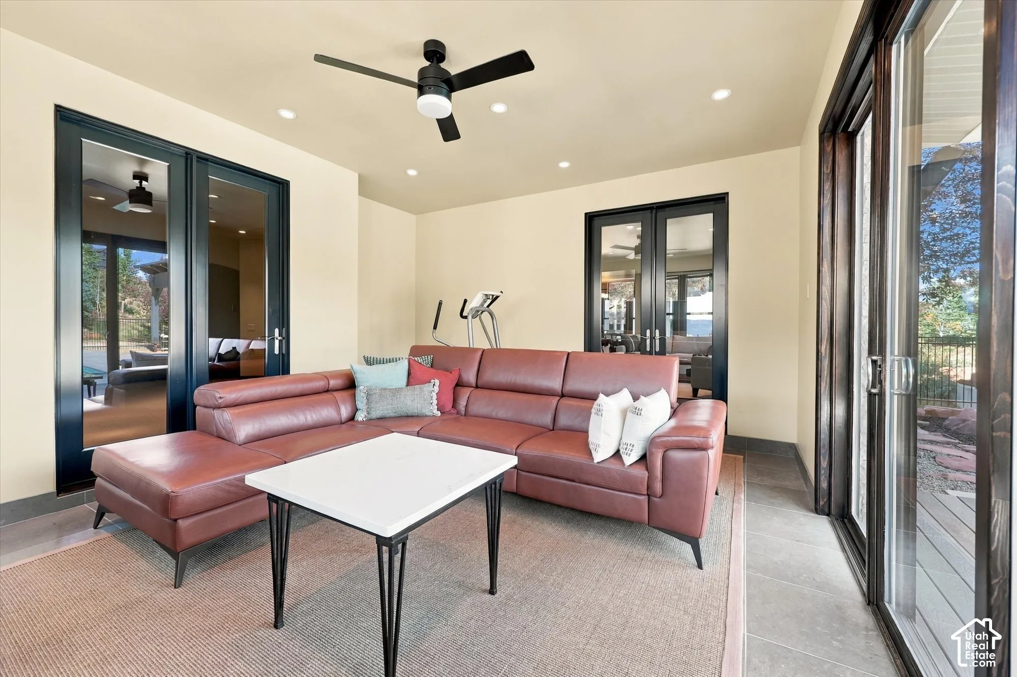 Covered patio featuring large-format tile flooring, recessed ceiling lighting, a matte black ceiling fan, and black-framed glass french and sliding doors