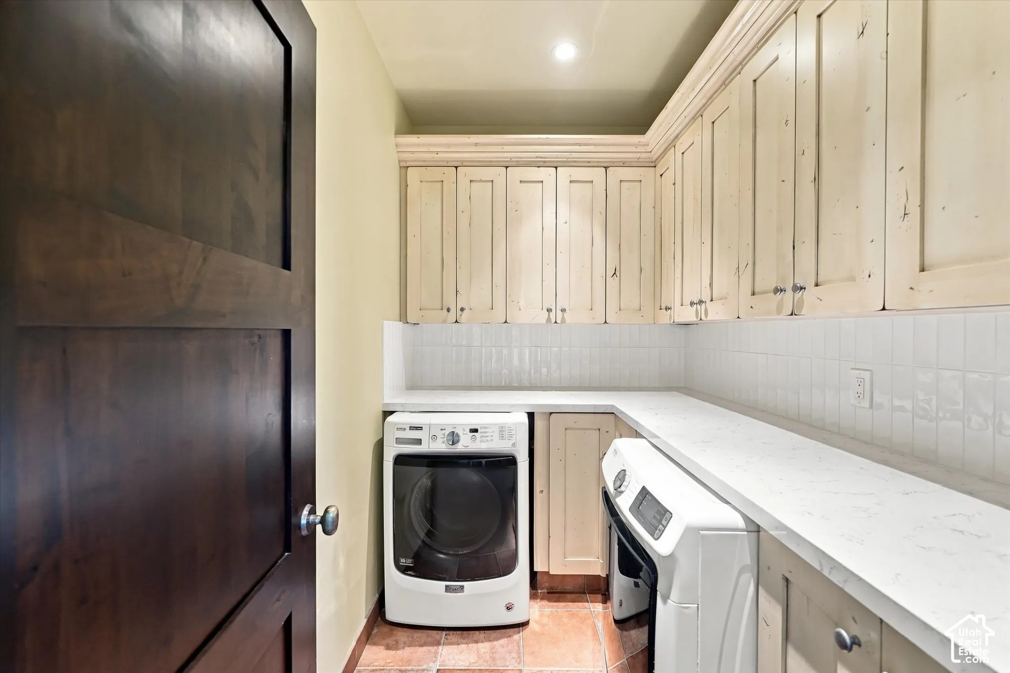 Laundry room featuring custom painted cabinetry, stone-finish countertops, subway tile backsplash, terra-cotta tile flooring, and a solid wood-finish door