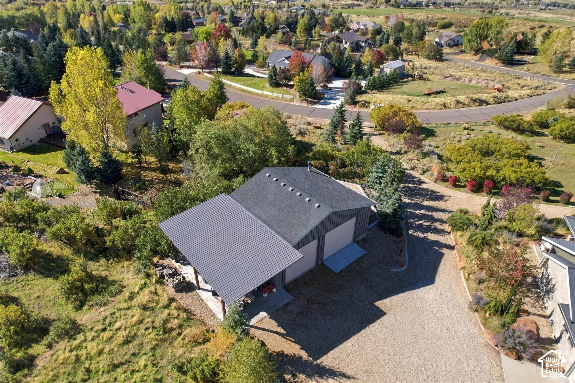 Detached multi-car garage featuring a shingle roof, integrated metal-paneled carport, and paved driveway, situated on a lot with mature trees and native landscaping