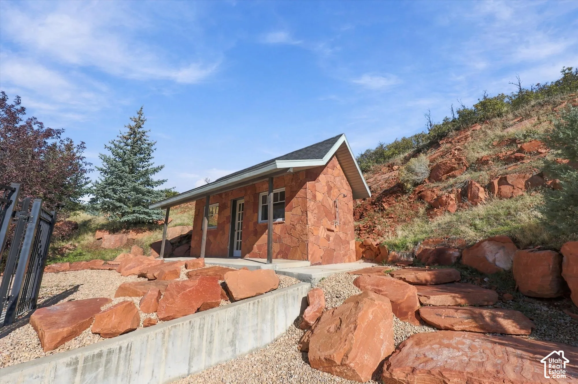 Detached structure featuring stone veneer siding, a covered porch, and a shingle roof, complemented by natural rock landscaping