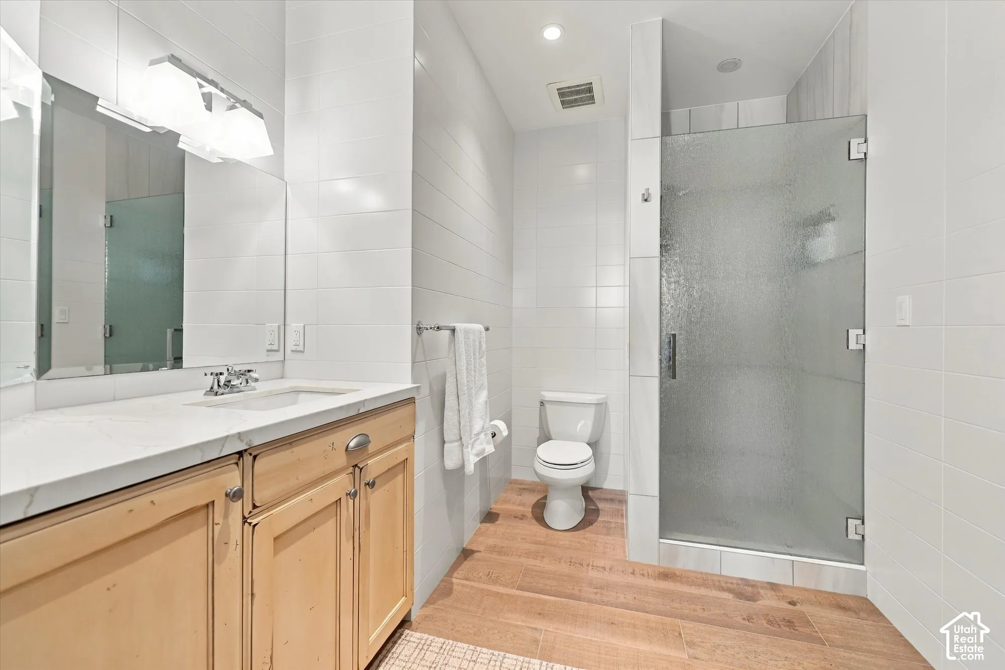 Bathroom featuring a wood-finish vanity with a stone countertop, an integrated sink, floor-to-ceiling tiled walls, and a glass-enclosed shower