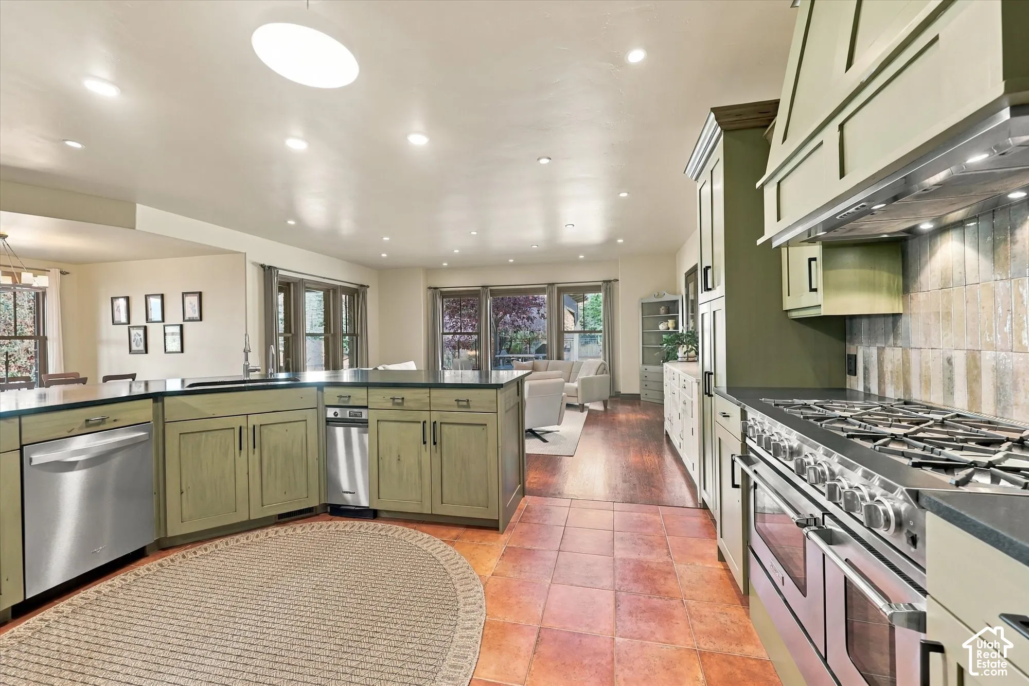 Kitchen featuring custom-colored cabinetry, stainless steel professional-grade range, built-in range hood, terracotta tile flooring, and stone countertops