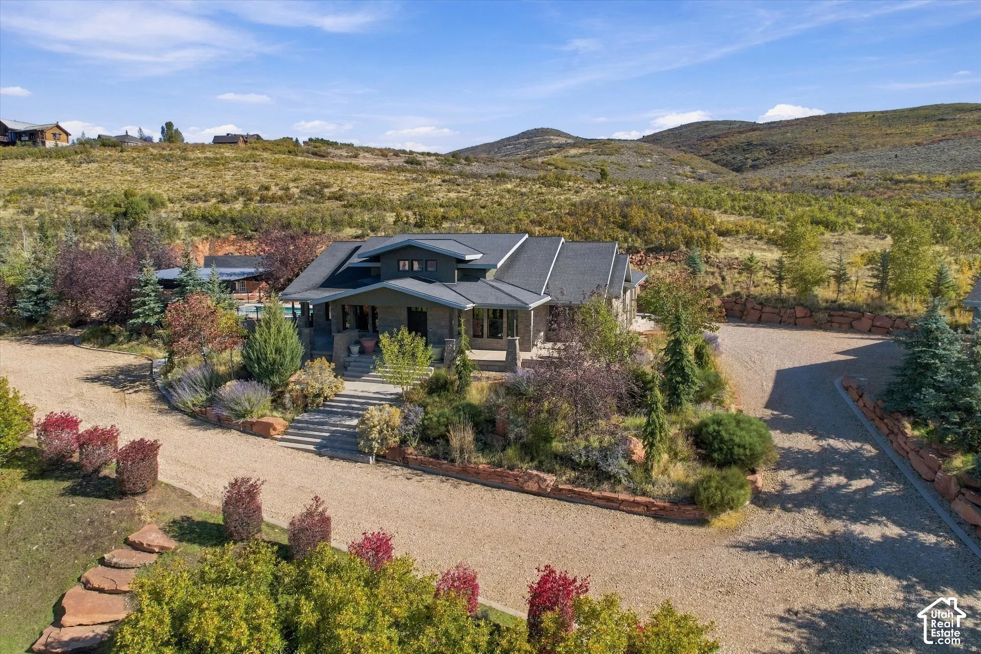 Multi-level exterior featuring stone and siding construction, covered entryway, tiered stone hardscaping, expansive gravel driveway, and surrounding mountainous landscape