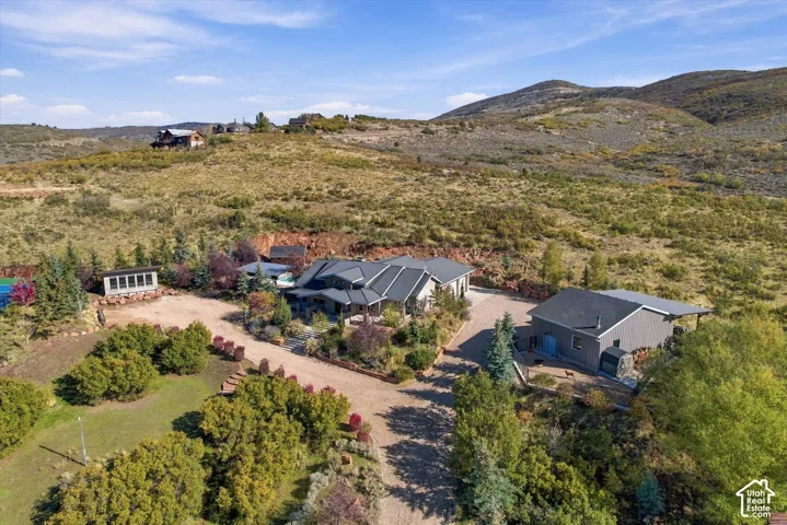 Extensive property featuring a multi-structure residence, detached garage, tennis court, sprawling landscaped grounds, and a mountain backdrop