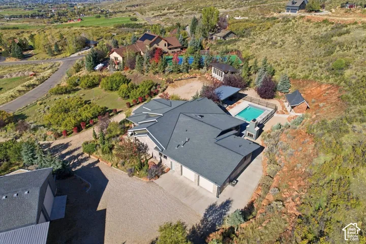 Aerial perspective featuring a multi-car garage, in-ground swimming pool, outdoor stone fireplace, and detached secondary structure on a hillside lot