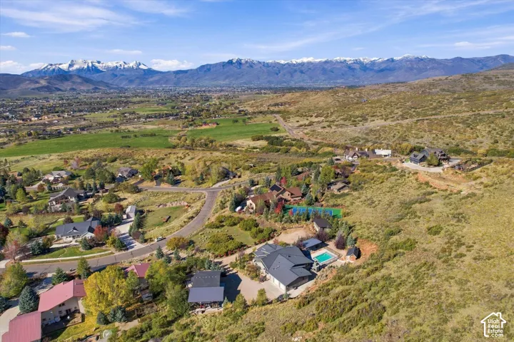 Aerial perspective of property featuring an expansive multi-level residence, private swimming pool, mountain backdrop, and hillside landscaping