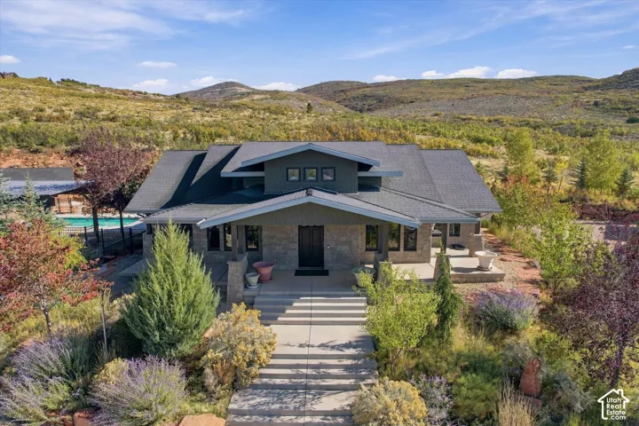 Craftsman-style residence featuring stone veneer siding, shingled roofing, concrete entry stairs, and a mountain landscape backdrop