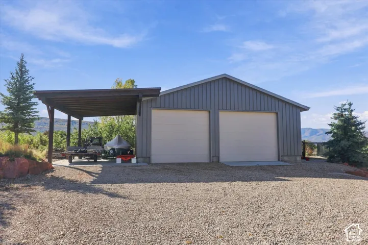 Detached metal-sided garage featuring two garage bays, a covered side carport, and a gravel driveway