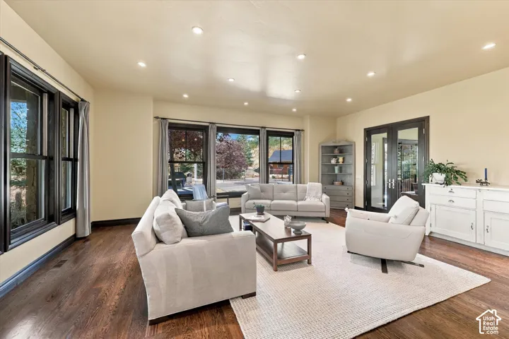 Spacious room featuring dark-finish wood flooring, recessed lighting, multi-pane windows with dark frames, and glass-paneled double doors