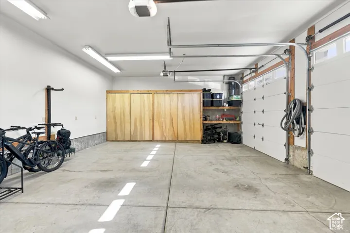 Multi-car garage featuring concrete flooring, built-in wooden storage cabinetry, integrated shelving, and overhead lighting fixtures