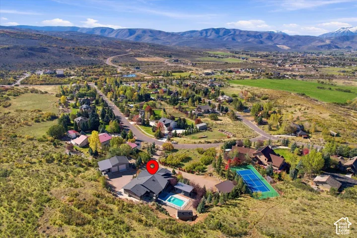 Aerial perspective of a multi-structure property featuring an inground swimming pool, a dedicated tennis court, a detached garage, and expansive mountain terrain