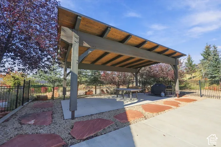 Covered outdoor pavilion featuring a timber-frame structure, concrete patio base, natural stone pavers, and perimeter metal fencing