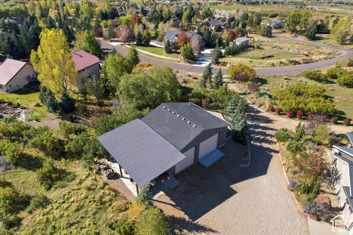 Detached multi-car garage featuring a shingle roof, integrated metal-paneled carport, and paved driveway, situated on a lot with mature trees and native landscaping