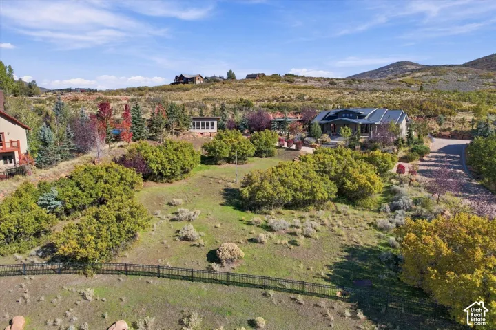 Expansive lot featuring mature trees, diverse native vegetation, a black metal perimeter fence, and mountain landscape backdrop