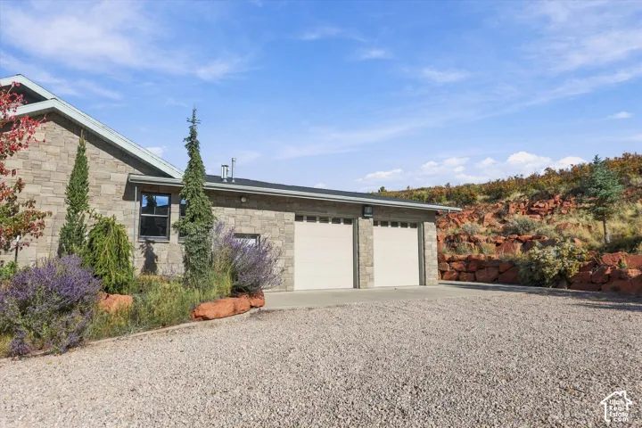 Stone masonry exterior, two-car garage with paneled doors, and gravel driveway set against a natural rock landscape