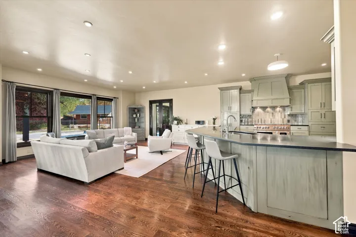 Open-concept living space featuring wood-finish flooring, recessed lighting, and a kitchen equipped with a curved island, custom cabinetry, and a professional-grade range with a built-in hood