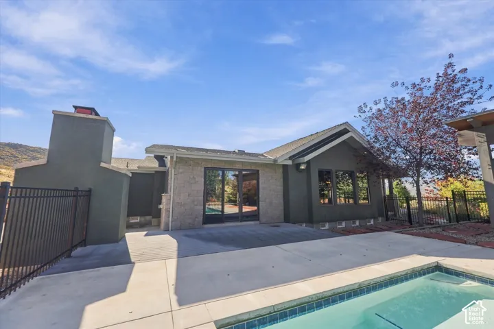 Exterior rear elevation featuring stucco siding, stone veneer accents, an inground pool with concrete decking, a metal perimeter fence, and sliding glass doors