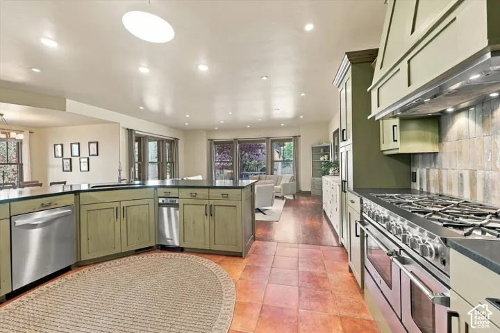 Kitchen featuring custom-colored cabinetry, stainless steel professional-grade range, built-in range hood, terracotta tile flooring, and stone countertops