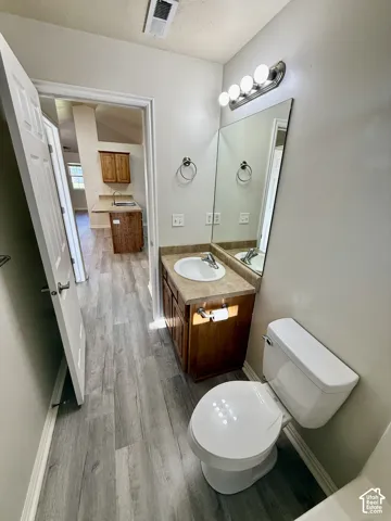 Bathroom featuring wood-finish flooring, a wood vanity with a stone-composite countertop, an integrated oval basin, and a wall-mounted light fixture
