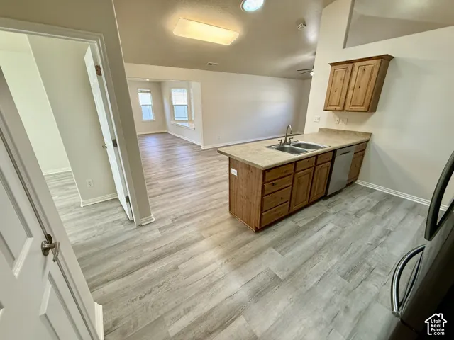 Open-concept kitchen featuring wood-finish cabinetry with ample storage, a stainless steel sink with countertop workspace, and wood-finish flooring throughout the main living area
