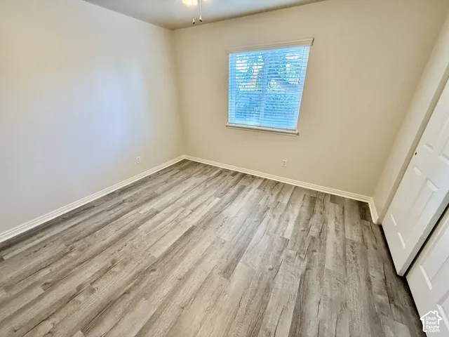 Neutral-toned interior featuring wood-finish flooring, a ceiling fan with integrated lighting, and a window with horizontal blinds