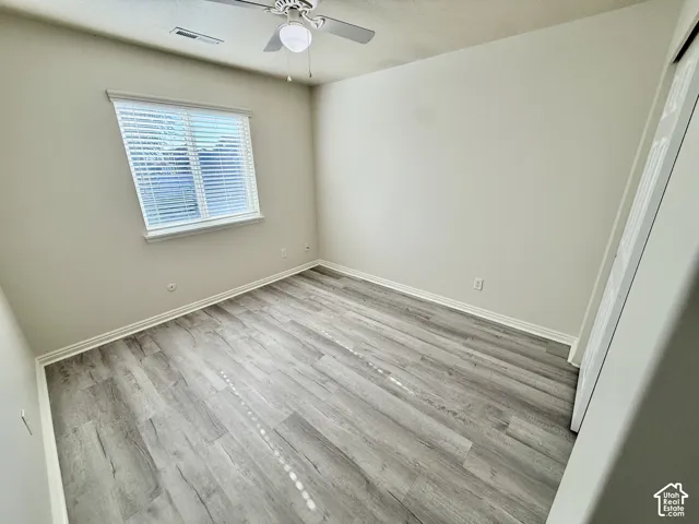 Neutral-toned interior featuring wood-finish flooring, a ceiling fan with integrated lighting, and a window with horizontal blinds