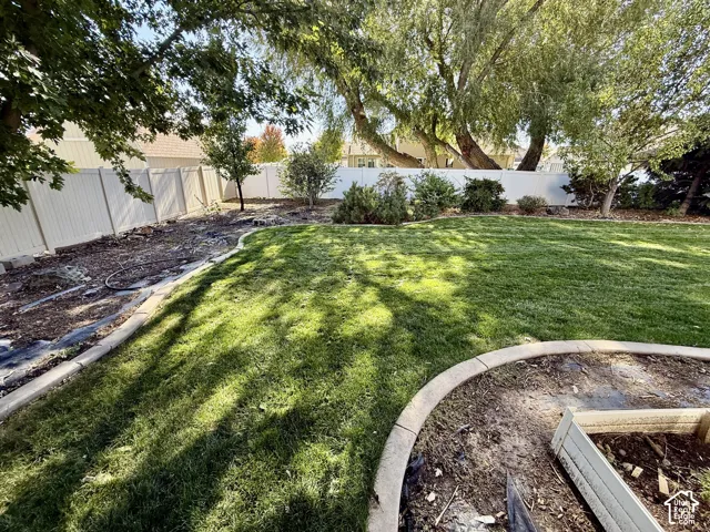 Expansive backyard featuring a lush, manicured lawn with mature shade trees, concrete edging, mulched landscape beds, and metal fencing along the perimeter