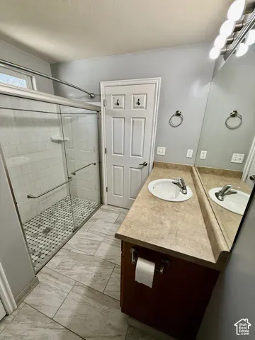 Bathroom featuring a glass-enclosed shower with tiled surround and mosaic floor, a vanity with a solid-surface countertop, and a large wall-mounted mirror