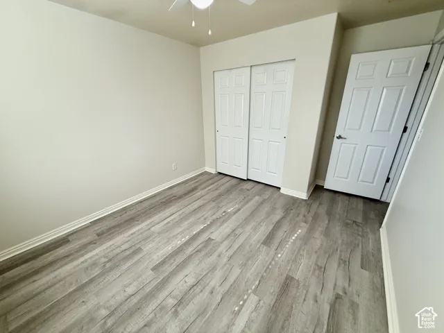 Room featuring wood-finish flooring, a six-panel closet door, a six-panel entry door, and a ceiling-mounted light fixture with fan