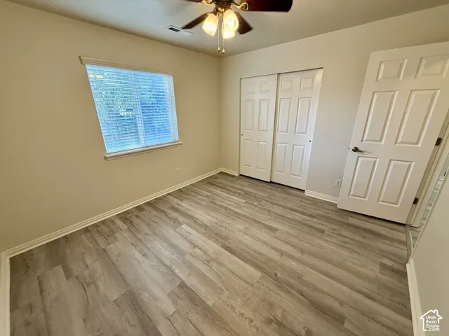 Wood-finish flooring, dual-panel closet doors, interior six-panel door, and a ceiling-mounted light fixture with a central fan