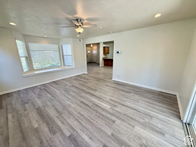 Spacious open-concept living area featuring wood-finish flooring throughout, recessed ceiling lighting, and a ceiling fan with integrated light fixture