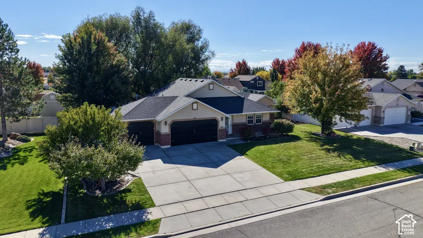 Aerial perspective of a multi-level residence featuring a multi-car garage, brick and siding exterior, concrete driveway, and mature landscaping