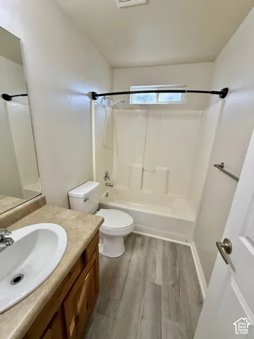 Bright and functional bathroom featuring a wood-finish vanity with an integrated sink, ceramic tile shower-tub combination with curved rod and enclosure, dual mirrors, and wood-finish flooring throughout