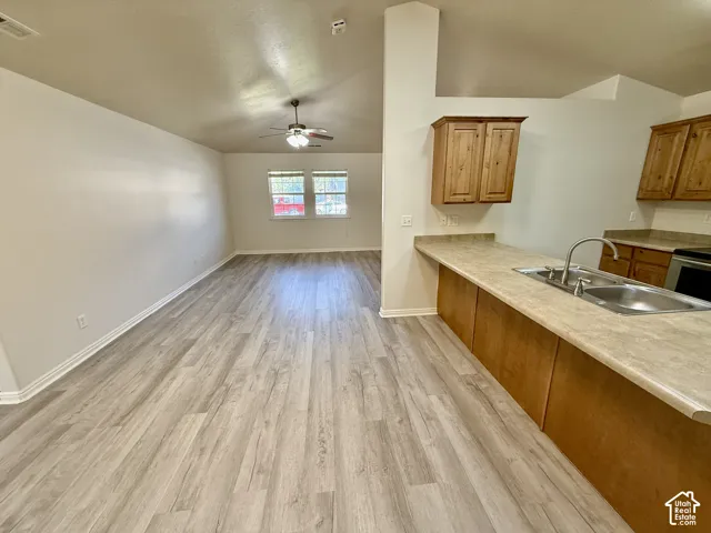 Wood-finish flooring, neutral walls, vaulted ceiling with a central fan, and kitchen featuring laminate countertops with a stainless steel sink