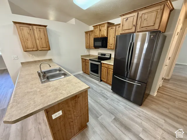 Kitchen featuring wood cabinetry, laminate countertops, stainless steel appliances, and wood-finish flooring