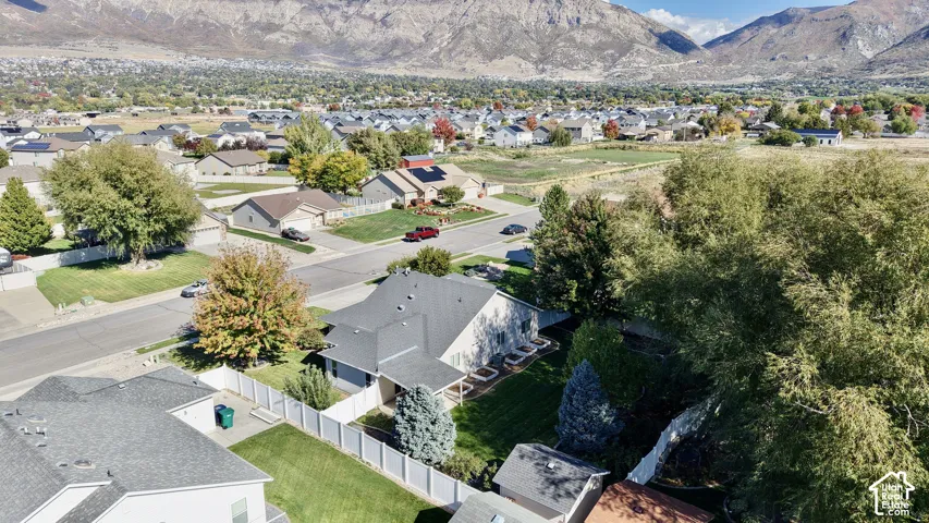 Aerial perspective featuring mountain scenery, mature trees, a fenced-in yard, raised garden beds, and an asphalt shingle roof