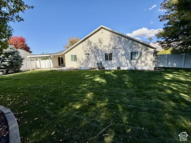 Spacious backyard featuring a manicured lawn, vinyl perimeter fencing, raised garden beds, and a covered patio area