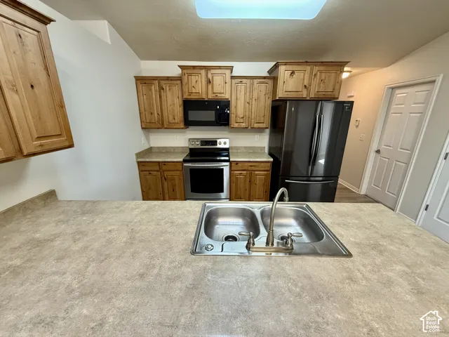 Kitchen featuring natural wood cabinetry, stone-patterned laminate countertops, stainless steel appliances, and a dual-basin sink with a gooseneck faucet