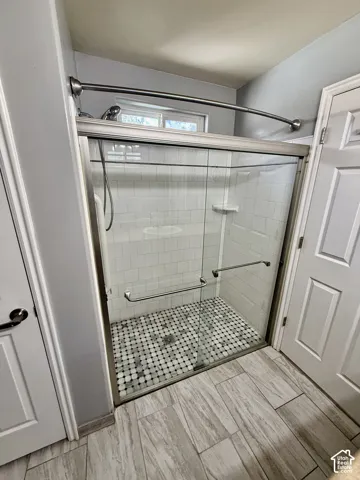 Walk-in shower featuring a sliding glass door, white subway tile surround, patterned mosaic tile flooring, and brushed nickel hardware