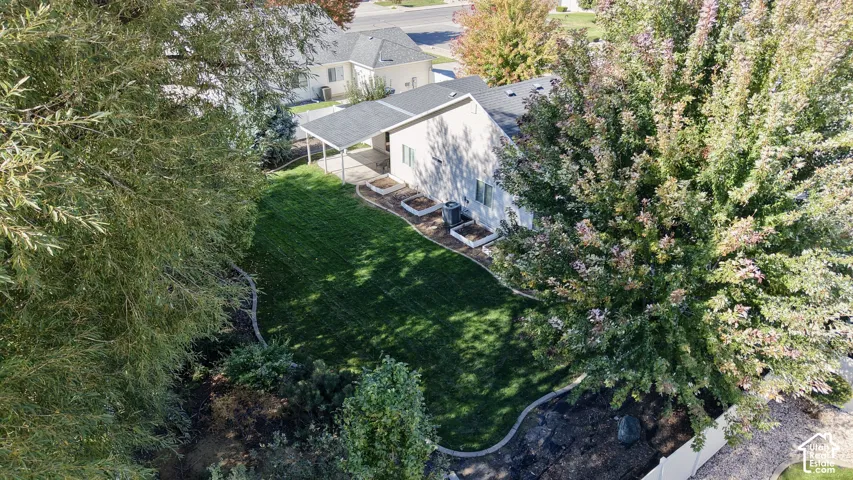 Backyard featuring a manicured lawn, mature trees, built-in raised garden beds, a concrete patio, and continuous concrete curbing