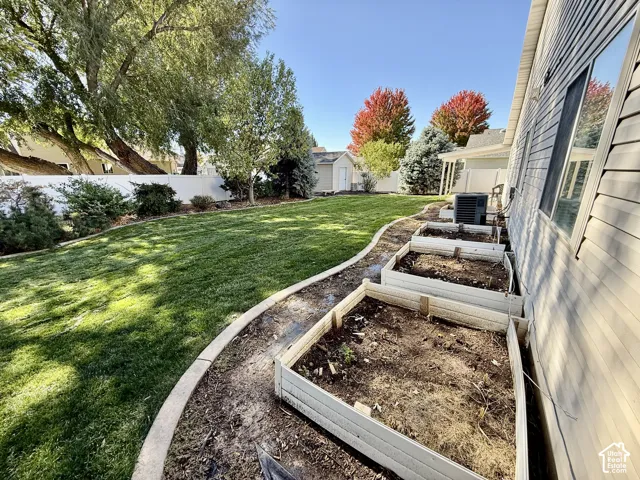 Backyard featuring a manicured lawn, raised garden beds, concrete landscape curbing, and a perimeter vinyl fence