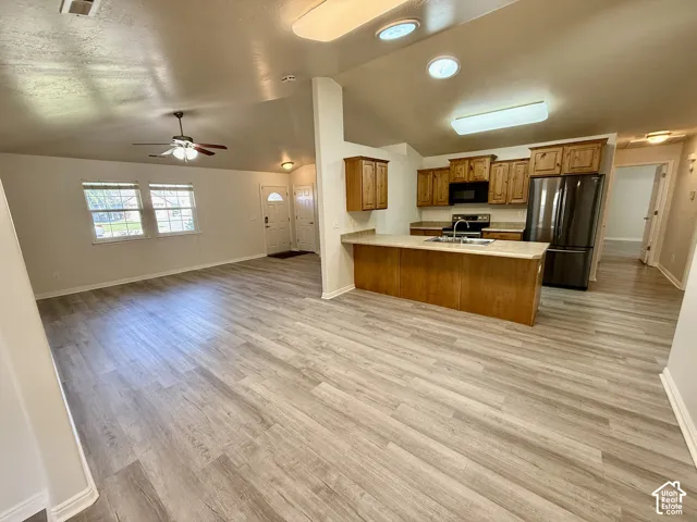 Open-concept interior featuring vaulted ceilings, wood-finish flooring, a kitchen peninsula with bar seating, and integrated ceiling lighting