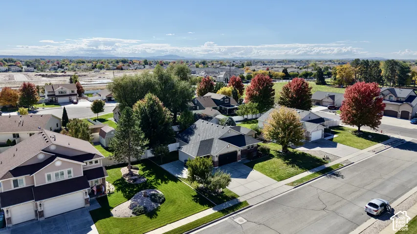 Aerial perspective of residential properties featuring multi-gabled roofs, attached multi-car garages, manicured lawns, and mature deciduous trees